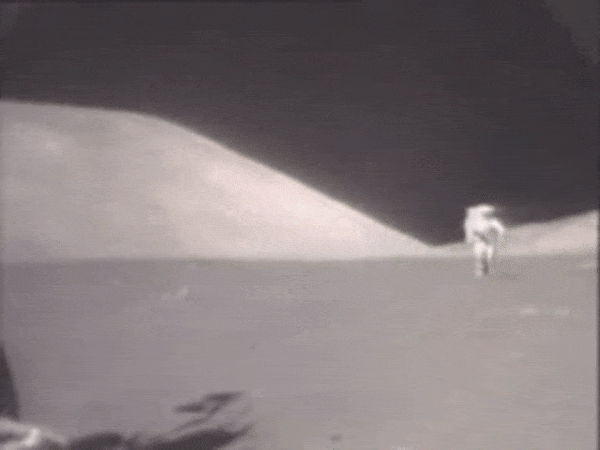 Человек,напоминающий астронавта скачет по поверхности,напоминающей лунную.