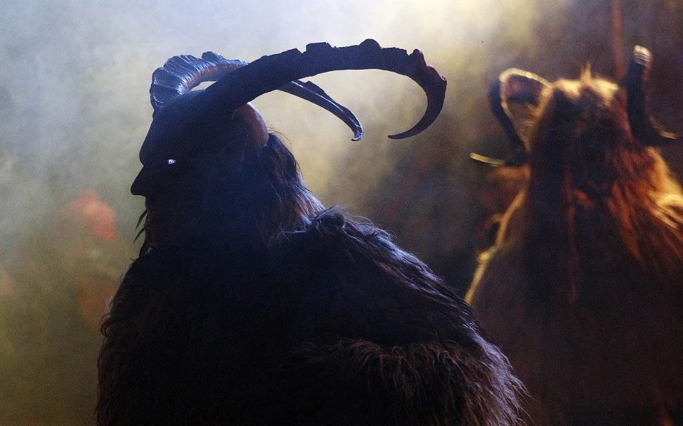 Человек в маске демона, которая сделана из кедрового дерева с козьими рогами