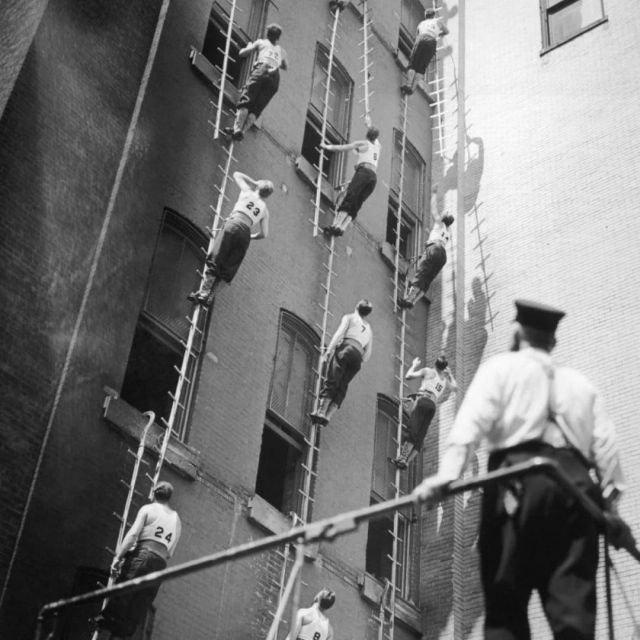 Около 1950 года в учебном центре Нью-Йорка пожарные-стажёры отрабатывают навыки подъема по стене здания.